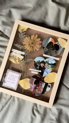 a shadow box with pictures and flowers in it sitting on a bed covered by gray sheets