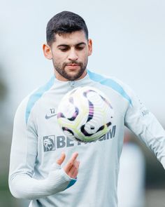 a man holding a soccer ball in his right hand and wearing a white shirt with blue sleeves