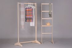 an open wooden rack with clothes and scarfs hanging from it's sides, against a gray background