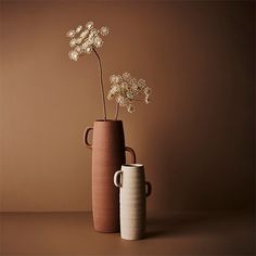 two vases with white flowers in them on a brown table next to each other