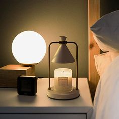 a night stand with a lit candle on it next to a bedside table and lamp