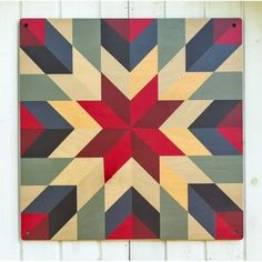 a colorful quilt hanging on the side of a white wooden building with wood planks