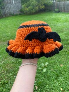 a crocheted orange and black hat on someone's arm in the grass