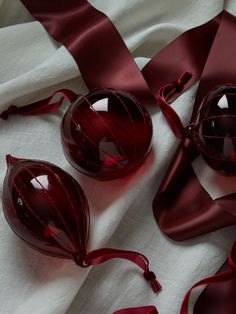 two red glass ornaments sitting on top of a white cloth covered tablecloth with ribbon around them