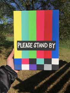 a hand holding up a piece of colored paper with the words please stand by on it