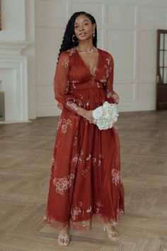 a woman in a red dress holding a white bouquet and standing on a wooden floor