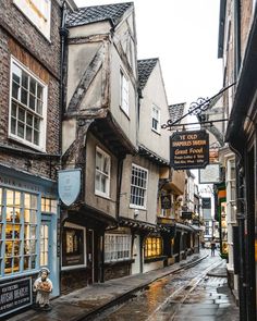 a wet street with old buildings and shops on the side, in an english town