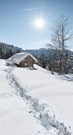 the sun shines brightly over a snowy mountain with a cabin in the foreground