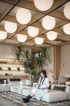 a woman is sitting on a couch in an office lobby with lights hanging from the ceiling