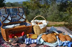 picnic food is laid out on an outdoor blanket in front of a basket with silverware and utensils