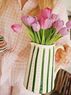 a woman holding a vase filled with pink tulips