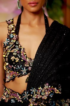 Black is your new summer romantics to go all glam for any intimate soiree of the season. This pre-draped saree highlighted with the lines of black bead-work all around comes with a dazzling floral blouse accentuated with embroidered multicolor bead-work and cut-work. The floral bead embroidery also highlights the waistline and goes on the pallu’s borders. Sleeveless blouse with a deep neck and cutwork detailing at the edges. Hook at the back of the blouse. The silk satin pre-draped saree is acce Black Saree With Multicolor Blouse, Saree Edging Ideas, Multicolor Blouse Design, Black Blouse Designs For Saree, Beads Work On Blouse, After Wedding Dress, Wedding Blouses, Organza Suit, Saree Drape