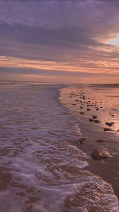 the sun is setting over the ocean with rocks in the foreground and waves on the shore