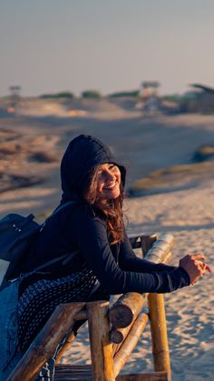 a woman sitting on a wooden bench at the beach