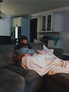 two people sitting on a couch with a blanket over their heads and one person holding a baby