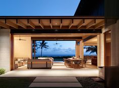 an outdoor living room and dining area is lit up at night with the ocean in the background