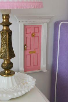 a pink door is in the background behind a white table with a lamp on it