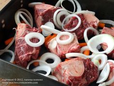 raw meat and onions being cooked in a roasting pan with tongs on the side