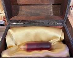 an open wooden box with a red object in it's lid and satin lining