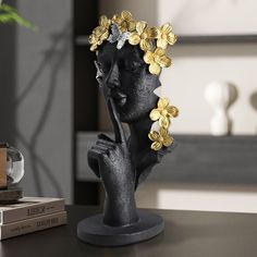 a statue of a woman with flowers in her hair sitting on a table next to books