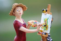 a figurine is holding a piece of art and painting on an easel