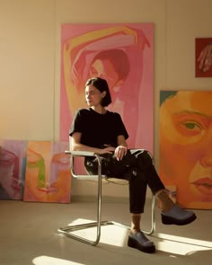 a woman sitting in a chair next to paintings