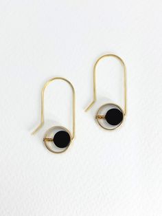 Golden brass and semi precious stones of Onyx are paired together in these geometric dangle earrings.  The matte black onyx stones, with their deep, velvety hue, compliment the warmth of the polished brass.  The brass gleams softly against the smooth surface of the onyx and the contrasting textures and tones create visual impact.  A rounded edge brass frame surrounds a coin shaped stone as a block of three small, gold plated, glass seed beads position it off centre.  Approximate measurements- 4c Modern Black Round Hoop Earrings, Minimalist Black Metal Jewelry, Modern Black Single Earring, Modern Black Hoop Earrings As Gift, Modern Black Hoop Earrings For Gift, Modern Black Hoop Earrings For Everyday, Modern Black Circular Jewelry, Modern Onyx Earrings With Black Enamel, Minimalist Black Round Hoop Earrings