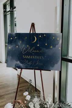 a welcome sign in front of a window with flowers and greenery on the floor