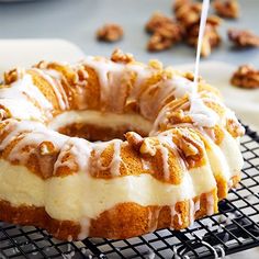 a bundt cake sitting on top of a cooling rack covered in icing and nuts