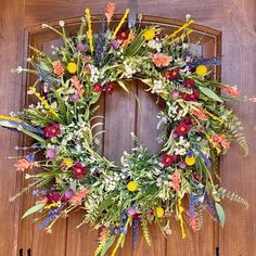 a wreath is hanging on the front door with flowers and greenery around it's edges