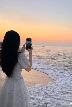 a woman standing on top of a beach holding a cell phone