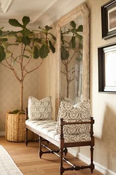 a bench with two pillows on it in front of a mirror and a potted plant