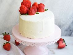 a white cake topped with strawberries on top of a pink cake stand next to some napkins