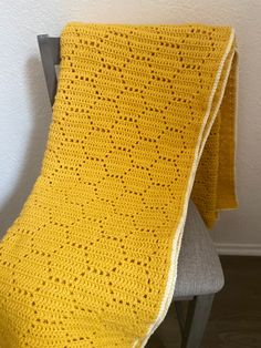 a yellow crocheted blanket sitting on top of a chair next to a white wall