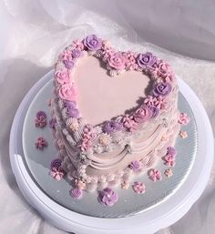 a heart shaped cake with pink and purple frosting on a platter covered in flowers