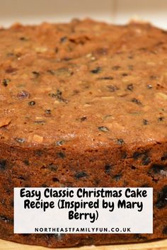 a cake sitting on top of a wooden cutting board next to a white sign that says easy classic christmas cake recipe inspired by mary berry