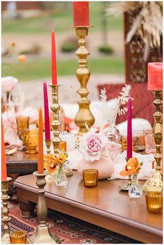 a table topped with lots of gold candles and flowers on top of it's wooden table