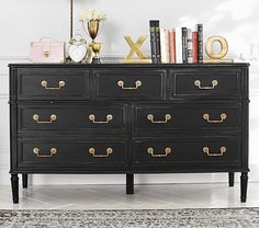 a black dresser with gold handles and letters on top, next to a white wall