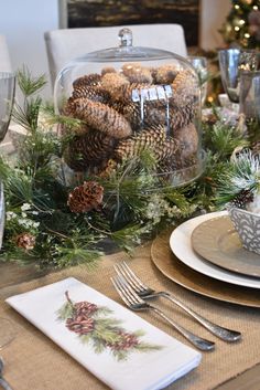 a dining room table set for christmas with pine cones and greenery