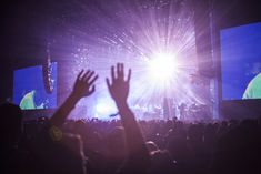 a crowd at a concert with their hands in the air and bright lights shining down on them