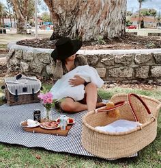 a woman sitting on top of a blanket next to a picnic basket filled with food