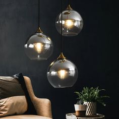 three clear glass globe lights hanging from the ceiling above a couch and coffee table in a dark room