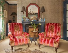 two red chairs sitting in front of a fire place next to a mirror on a wall