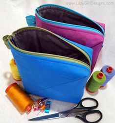 three zippered pouches sitting on top of each other next to scissors and thread