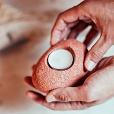 two hands holding a small pink object with a candle in it's center,