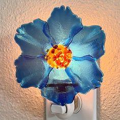 a blue flower shaped glass light switch cover on a white wall with a yellow center