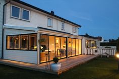 a house that is lit up at night with lights on the porch and windows open