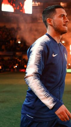 a man standing on top of a soccer field in front of a fire filled stadium