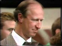 a man wearing a suit and tie standing in front of other people looking at something