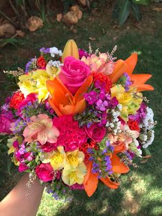 a bouquet of colorful flowers is held in someone's hand on the grass outside